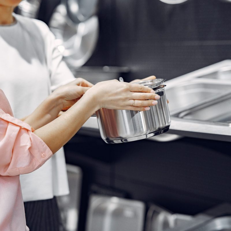 Woman examines various items of dishes. Beautiful woman shopping tableware in supermarket. Manager helps a costumer.